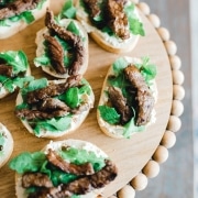 Steak crostini bites on beaded serving board.