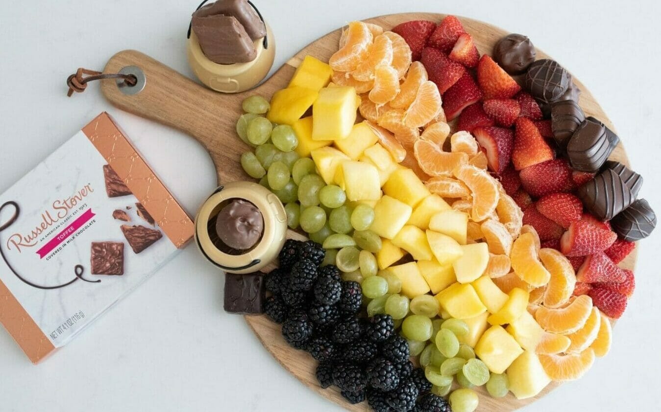 Rainbow of fruits and chocolates on snack board.